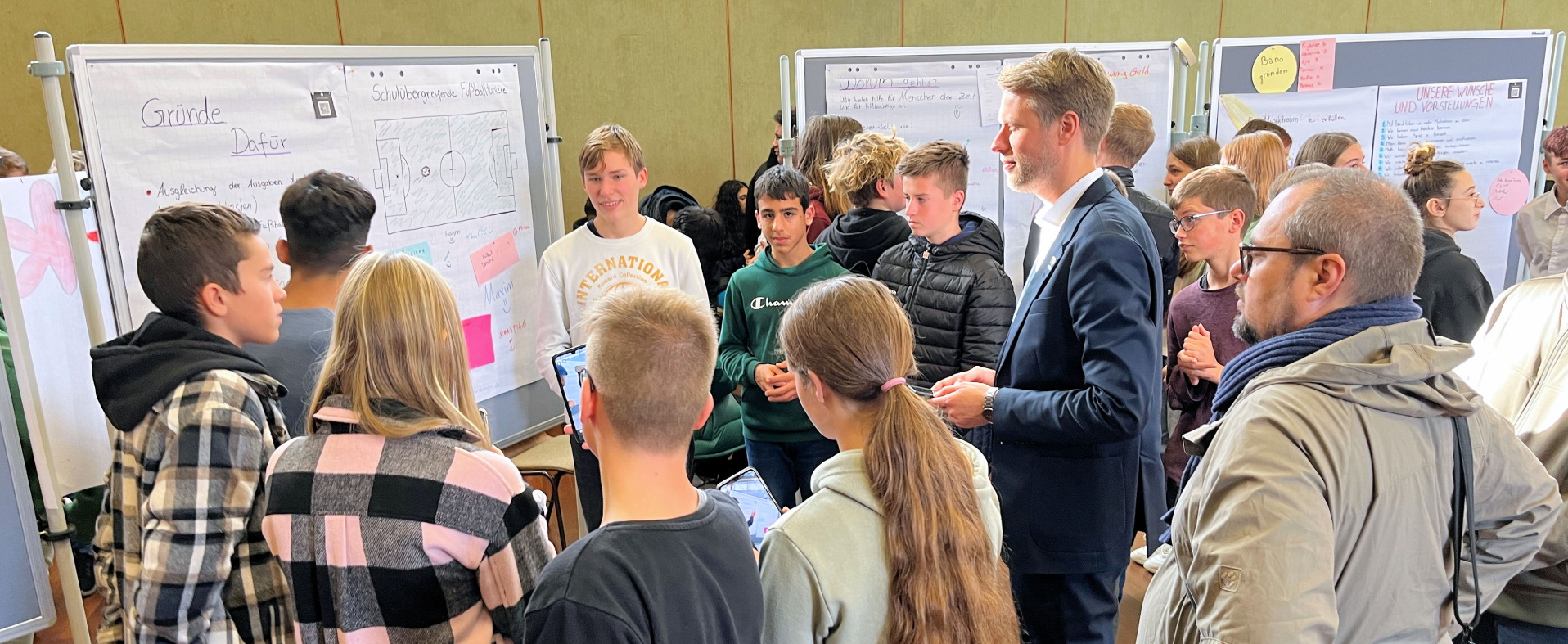Oberbürgermeister Markus Herrerea Torrez steht gemeinsam mit vielen Schülern vor einer Stellwand und sieht sich ein Plakat an, das von den Schülerinnen und Schülern gestaltet wurde. von