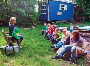 Kinder sitzen auf einer Bank, hören gespannt einer Erzieherin zu