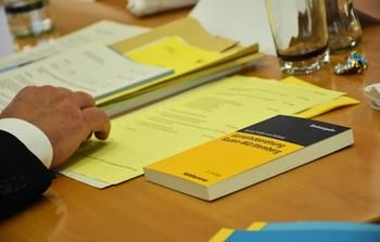 Symbolbild Gemeinderatssitzung: Hände auf dem Tisch mit gelben Vorlagen und der Gemeindeordnung Baden-Württembeg.