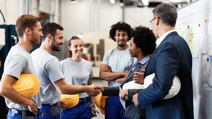 Vier Arbeitnehmer und ein Abteilungsleiter heißen eine neue Mitarbeiterin mit einem Handschlag willkommen